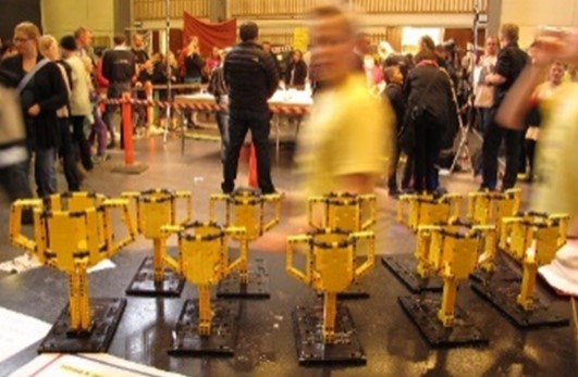 Finalepokalerne, der er bygget af LEGO Klodser. I baggrunden ser man slørede deltagere ved en tidligere finale i FIRST LEGO League.